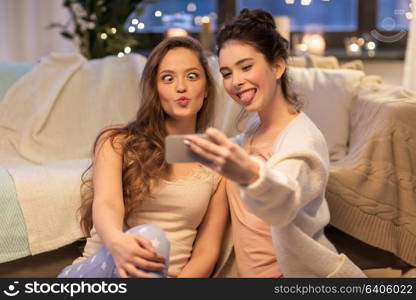 friendship, hygge and technology concept - happy female friends or teenage girls taking selfie by smartphone at home. female friends taking selfie by smartphone at home