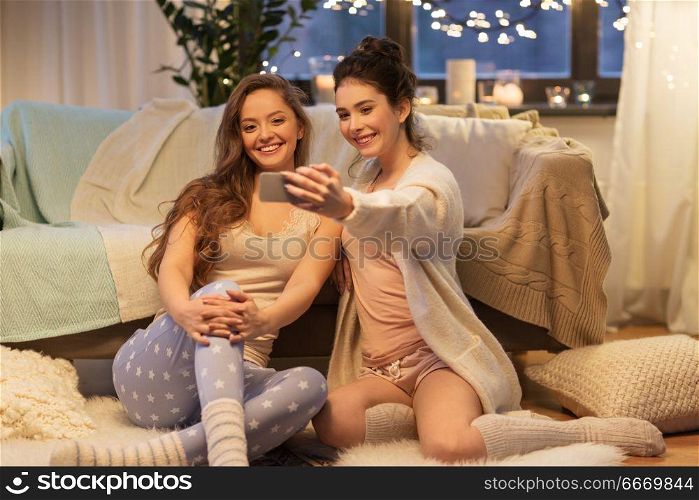 friendship, hygge and technology concept - happy female friends or teenage girls taking selfie by smartphone at home. female friends taking selfie by smartphone at home. female friends taking selfie by smartphone at home