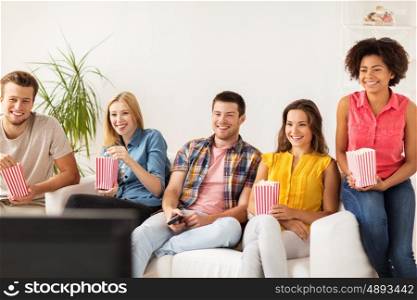 friendship, junk food, people and entertainment concept - happy friends eating popcorn and watching tv at home