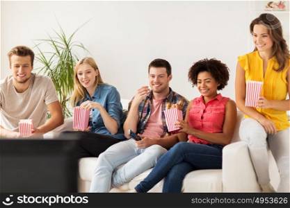 friendship, junk food, people and entertainment concept - happy friends eating popcorn and watching tv at home. happy friends with popcorn watching tv at home