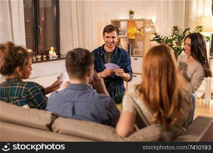 friendship, leisure and entertainment concept - happy friends playing cards game and drinking beer at home in evening. friends playing cards and drinking beer at home