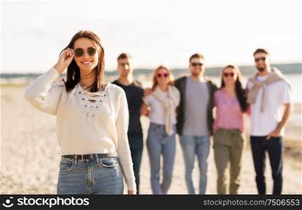 friendship, leisure and eyewear concept - happy woman in sunglasses with group of friends on beach in summer. happy woman with friends on beach in summer
