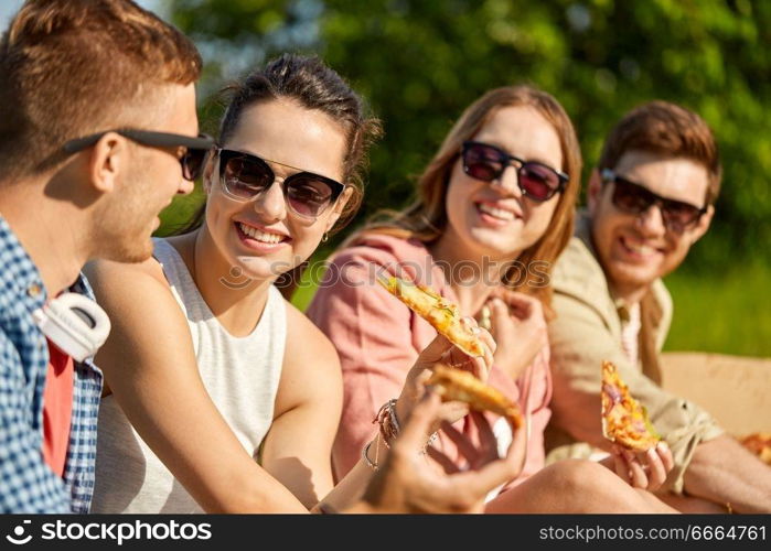 friendship, leisure and food concept - group of smiling friends eating pizza at picnic in summer park. friends eating pizza at picnic in summer park