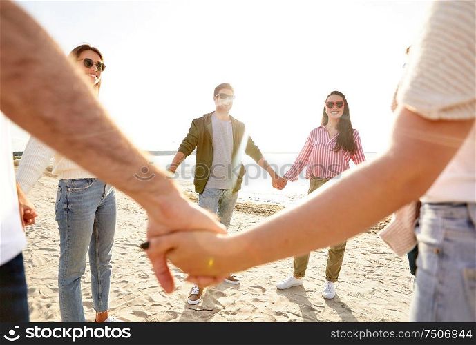 friendship, leisure and people concept - group of happy friends holding hands on beach in summer. happy friends holding hands on summer beach