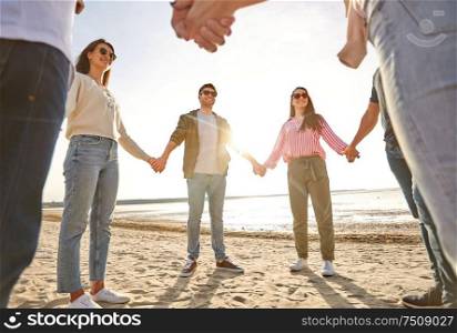 friendship, leisure and people concept - group of happy friends holding hands on beach in summer. happy friends holding hands on summer beach