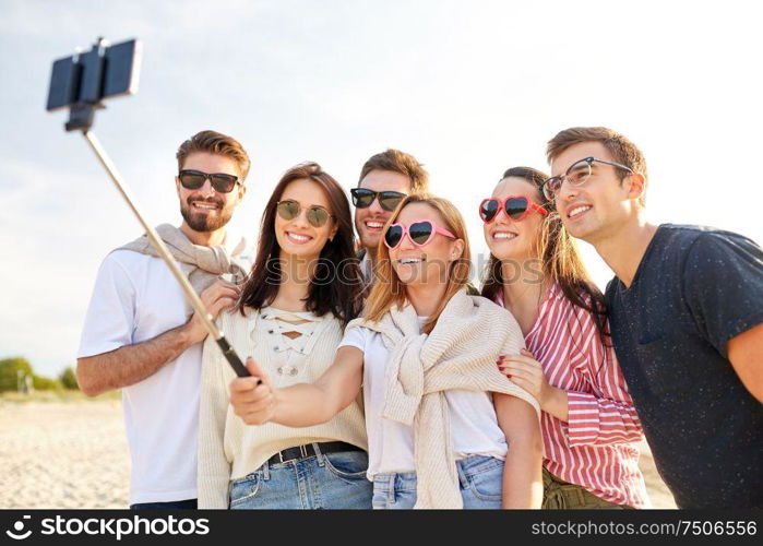 friendship, leisure and people concept - group of happy friends taking picture by smartphone on selfie stick on beach in summer. happy friends taking selfie on summer beach