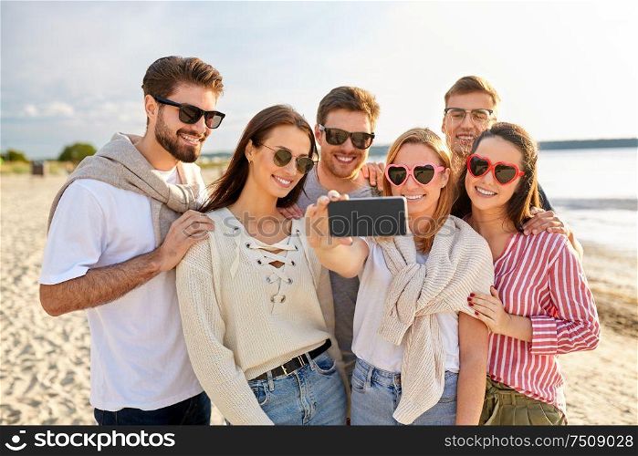 friendship, leisure and people concept - group of happy friends taking selfie by smartphone on beach in summer. happy friends taking selfie on summer beach