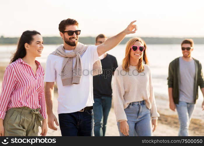 friendship, leisure and people concept - group of happy friends walking along beach in summer. happy friends walking along summer beach