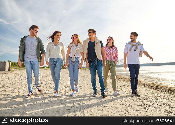 friendship, leisure and people concept - group of happy friends walking along beach in summer. happy friends walking along summer beach
