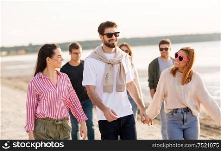 friendship, leisure and people concept - group of happy friends walking along beach in summer. happy friends walking along summer beach