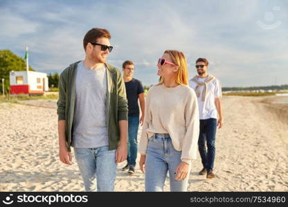 friendship, leisure and people concept - group of happy friends walking along beach in summer. happy friends walking along summer beach