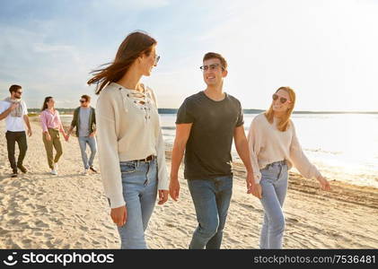 friendship, leisure and people concept - group of happy friends walking along beach in summer. happy friends walking along summer beach