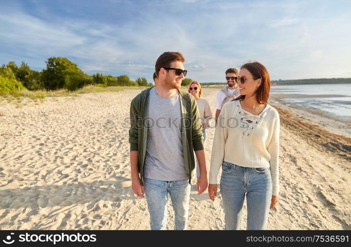 friendship, leisure and people concept - group of happy friends walking along beach in summer. happy friends walking along summer beach