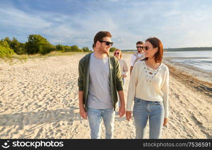 friendship, leisure and people concept - group of happy friends walking along beach in summer. happy friends walking along summer beach