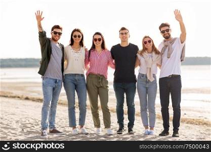 friendship, leisure and people concept - group of happy friends waving hands on beach in summer. happy friends waving hands on beach in summer