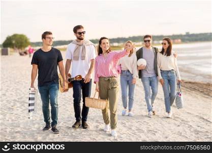 friendship, leisure and people concept - group of happy friends with guitar, chair and picnic basket walking along beach in summer. happy friends walking along summer beach