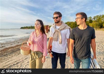 friendship, leisure and people concept - group of happy friends with guitar, picnic basket and folding chair walking along beach in summer. happy friends walking along summer beach