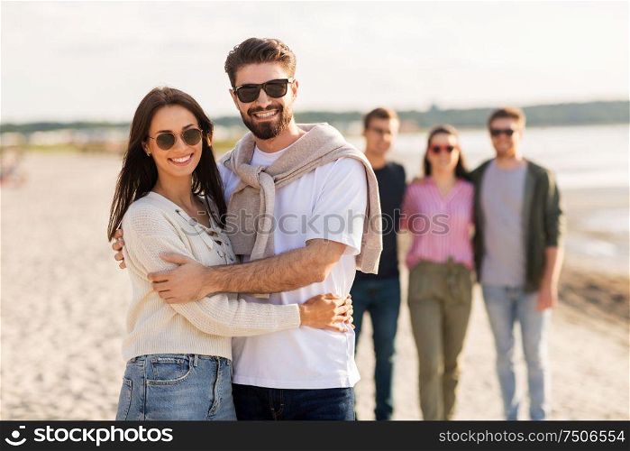 friendship, leisure and people concept - happy couple with group of friends hugging on beach in summer. happy couple with friends on beach in summer