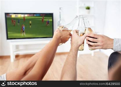 friendship, leisure and people concept - happy friends or soccer fans clinking non-alcoholic beer bottles and watching football game on tv at home. friends with beer watching football or soccer game