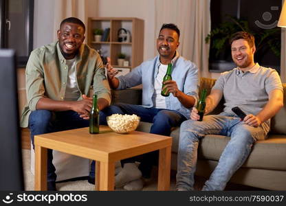 friendship, leisure and people concept - happy male friends with beer and popcorn watching tv at home at night. happy male friends with beer watching tv at home