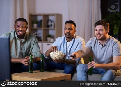friendship, leisure and people concept - happy male friends with beer and popcorn watching tv at home at night. happy male friends with beer watching tv at home