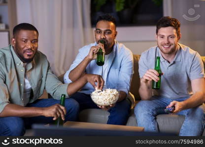 friendship, leisure and people concept - happy male friends with beer and popcorn watching tv at home at night. happy male friends with beer watching tv at home