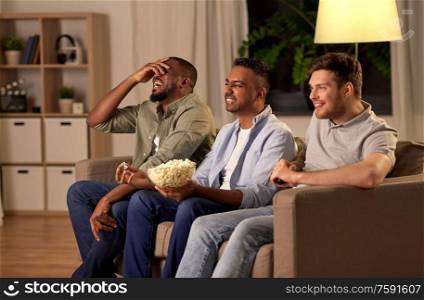 friendship, leisure and people concept - happy male friends with popcorn watching tv at home at night. male friends with popcorn watching tv at home