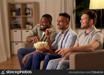 friendship, leisure and people concept - happy male friends with popcorn watching tv at home at night. male friends with popcorn watching tv at home