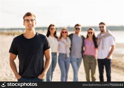 friendship, leisure and people concept - happy man in glasses with group of friends on beach in summer. happy man with friends on beach in summer