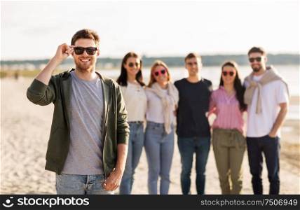 friendship, leisure and people concept - happy man in sunglasses with group of friends on beach in summer. man in sunglasses with friends on beach in summer
