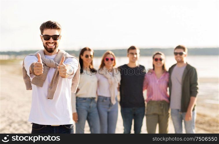 friendship, leisure and people concept - happy man with group of friends on beach in summer showing thumbs up. happy man with friends on beach showing thumbs up