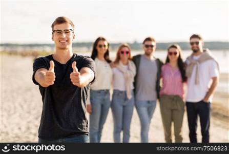 friendship, leisure and people concept - happy man with group of friends on beach in summer showing thumbs up. happy man with friends on beach showing thumbs up