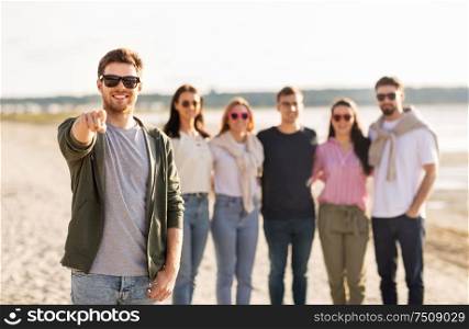 friendship, leisure and people concept - happy man with group of friends on beach in summer pointing finger to you. happy man with friends on beach in summer