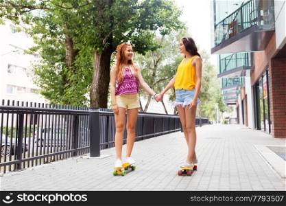 friendship, leisure and people concept - happy teenage girls or friends riding skateboards and holding hands on city street in summer. teenage girls riding skateboards in city