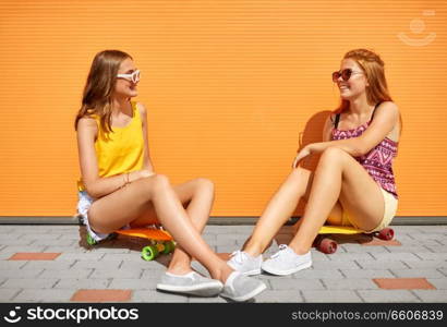 friendship, leisure and people concept - happy teenage girls or friends with short skateboards on city street in summer. teenage girls with short skateboards in city