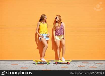 friendship, leisure and people concept - happy teenage girls or friends with short skateboards on city street in summer. teenage girls with short skateboards in city