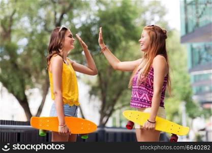 friendship, leisure and people concept - happy teenage girls or friends with short skateboards making high five on city street in summer. teenage girls with skateboards making high five