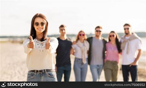 friendship, leisure and people concept - happy woman in sunglasses with group of friends on beach in summer showing thumbs up. woman with friends on beach showing thumbs up