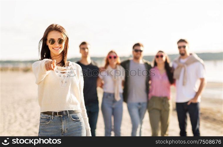 friendship, leisure and people concept - happy woman in sunglasses with group of friends on beach in summer pointing to you. happy woman with friends on beach pointing to you