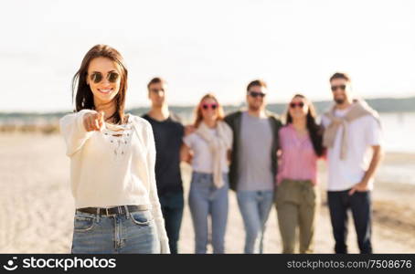 friendship, leisure and people concept - happy woman in sunglasses with group of friends on beach in summer pointing to you. happy woman with friends on beach pointing to you