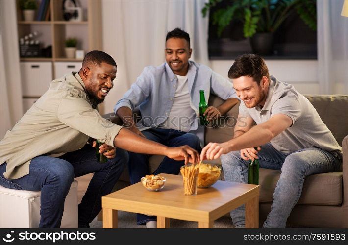 friendship, leisure and people concept - male friends drinking beer and eating crisps at home at night. male friends drinking beer with crisps at home