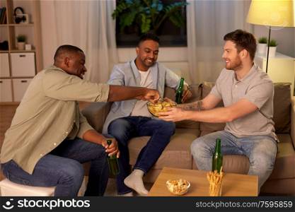 friendship, leisure and people concept - male friends drinking beer and eating crisps at home at night. male friends drinking beer with crisps at home