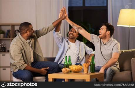 friendship, leisure and people concept - male friends drinking beer and making high five gesture at home at night. male friends with beer making high five at home