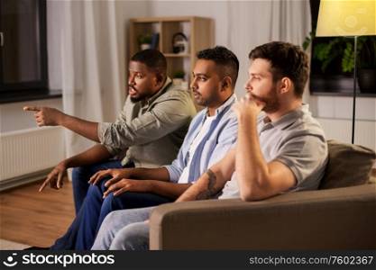 friendship, leisure and people concept - male friends watching tv and talking at home. male friends watching tv and talking at home
