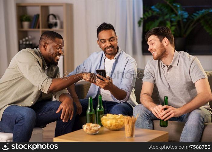 friendship, leisure and people concept - male friends with smartphone drinking beer at home at night. male friends with smartphone drinking beer at home