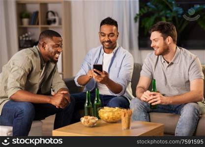 friendship, leisure and people concept - male friends with smartphone drinking beer at home at night. male friends with smartphone drinking beer at home