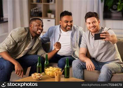 friendship, leisure and people concept - male friends with smartphone taking selfie and drinking beer at home at night. male friends with smartphone taking selfie at home