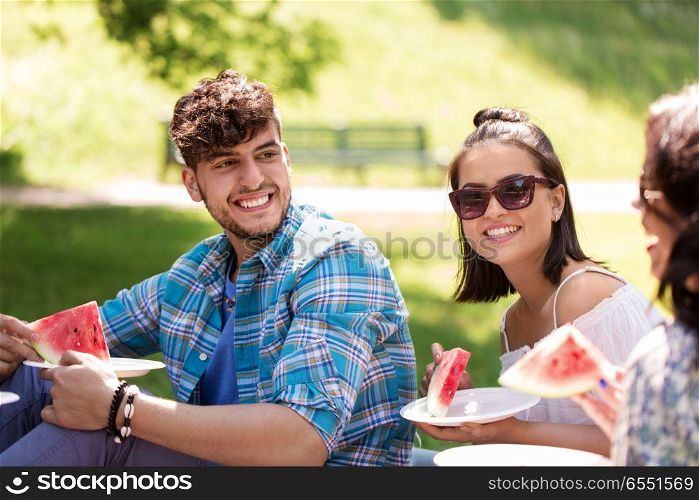 friendship, leisure and summer concept - group of happy friends eating watermelon at picnic in park. happy friends eating watermelon at summer picnic. happy friends eating watermelon at summer picnic