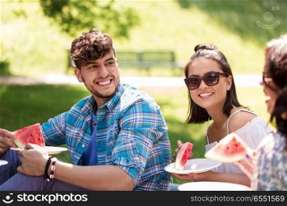 friendship, leisure and summer concept - group of happy friends eating watermelon at picnic in park. happy friends eating watermelon at summer picnic. happy friends eating watermelon at summer picnic