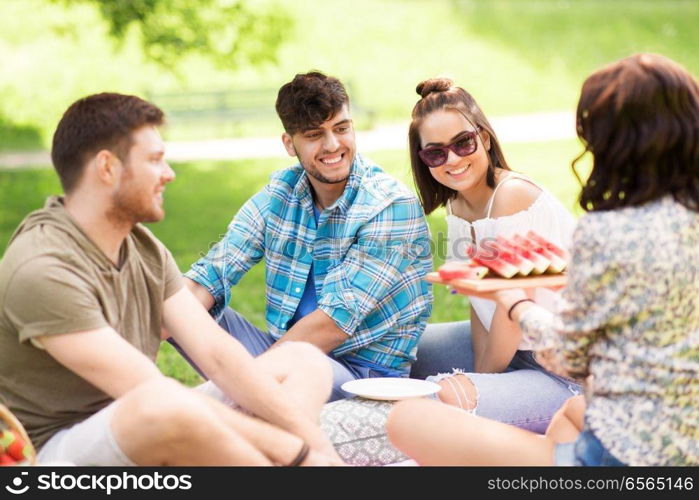 friendship, leisure and summer concept - group of happy friends eating watermelon at picnic in park. happy friends eating watermelon at summer picnic